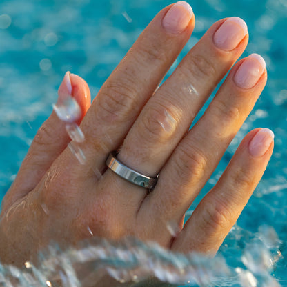 RingPay's Limited Edition Steel Payment ring worn on a person's ring finger, shown close-up with water droplets splashing in front of a bright blue swimming pool background.