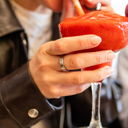 A close-up lifestyle shot of a person holding a red frozen drink in a stemmed glass, wearing RingPay's Limited Edition Steel Payment Ring.
