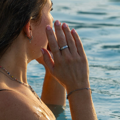 A woman in shallow water wearing RingPay's Limited Edition Steel Payment Ring on her left hand, with her face partially covered by her hand.